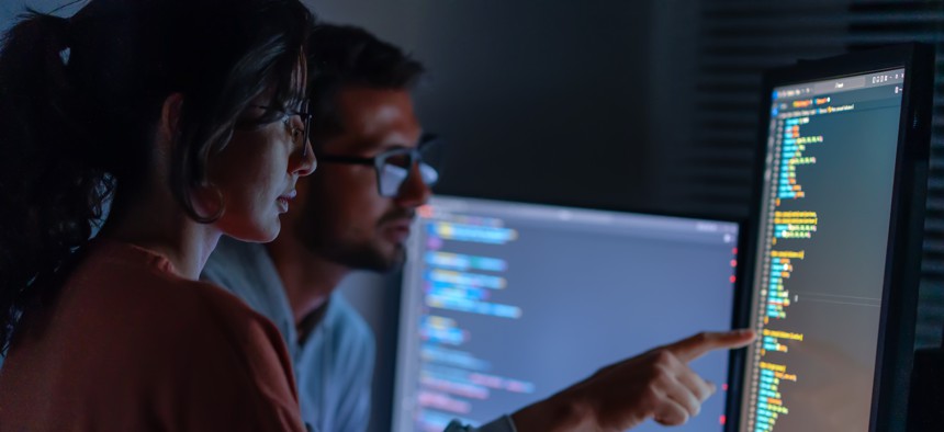 Two people working on a computer with code on the screen.